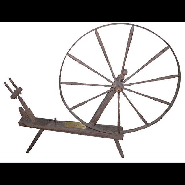 A color photograph of a wooden spinning wheel. The wheel is attached to the base with metal hardware. The bobbin faces left. 
